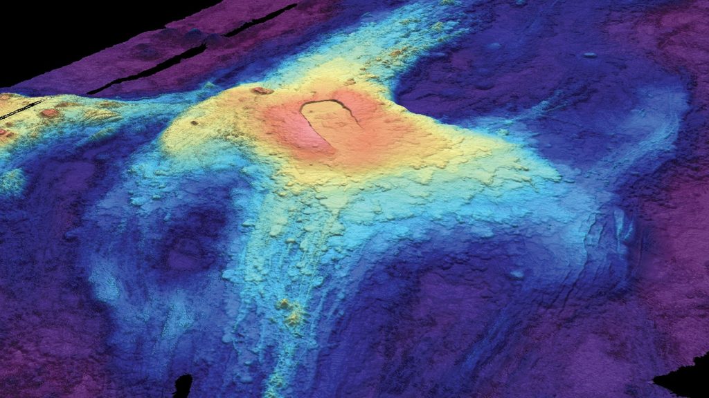 Una mappa batimetrica 3D (del fondale marino) dell'Axial Seamount del luglio 2014 mostra i flussi di lava delle eruzioni precedenti. Il rosso indica la lava alla massima elevazione sopra il fondale marino, mentre il blu scuro ai bordi mostra dove il flusso di lava era più sottile. 