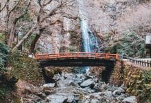 un ponte giapponese sotto una cascata, contornato di rocce e alberi tipici della cultura e tradizione giapponese