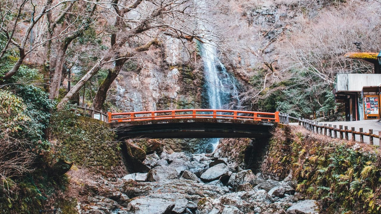 un ponte giapponese sotto una cascata, contornato di rocce e alberi tipici della cultura e tradizione giapponese