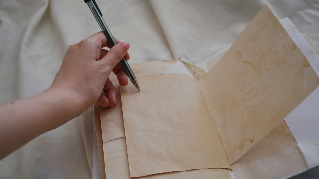 una mano che scrive su un foglio, la mano è chiaramente la sinistra che indica utilizzatore mancino