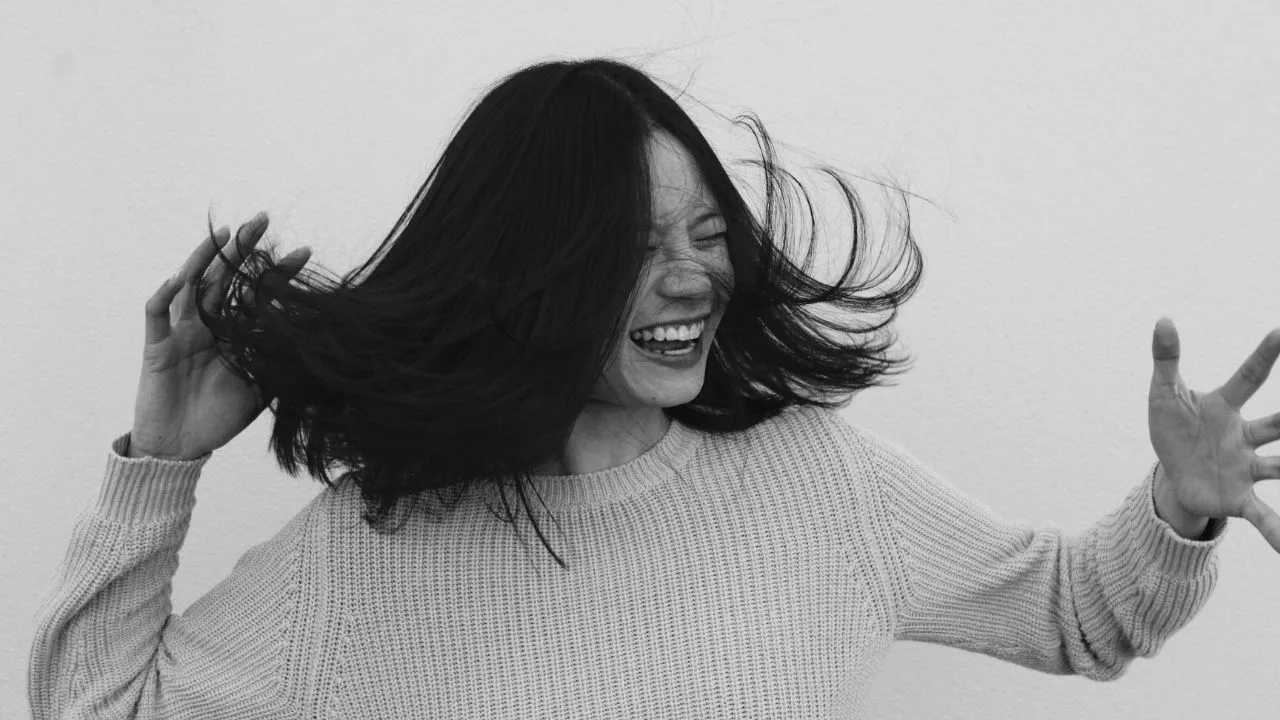 una donna asiatica che ride di gusto, con capelli a caschetto neri e un maglione chiaro