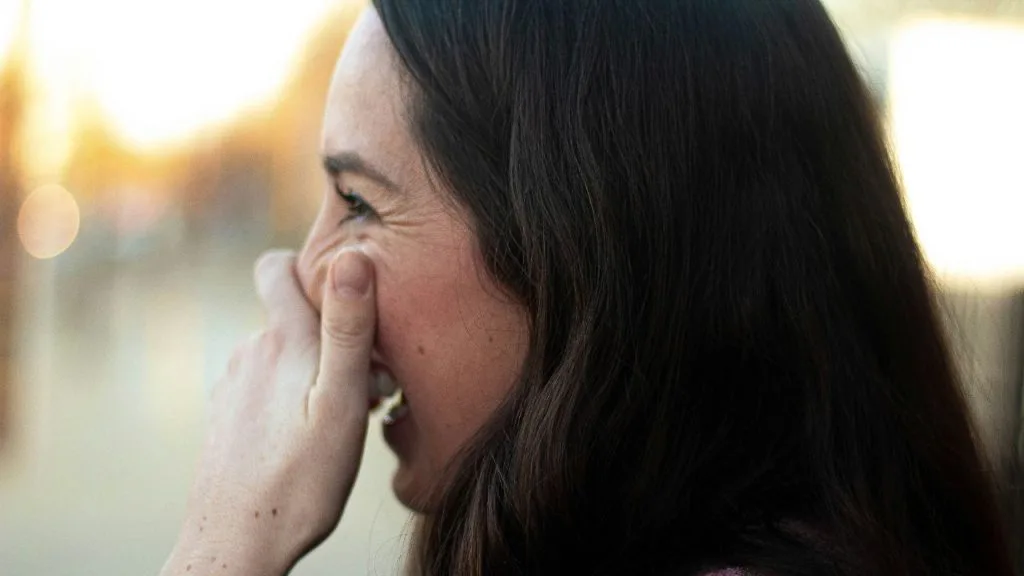 une fille riant avec la main devant la bouche