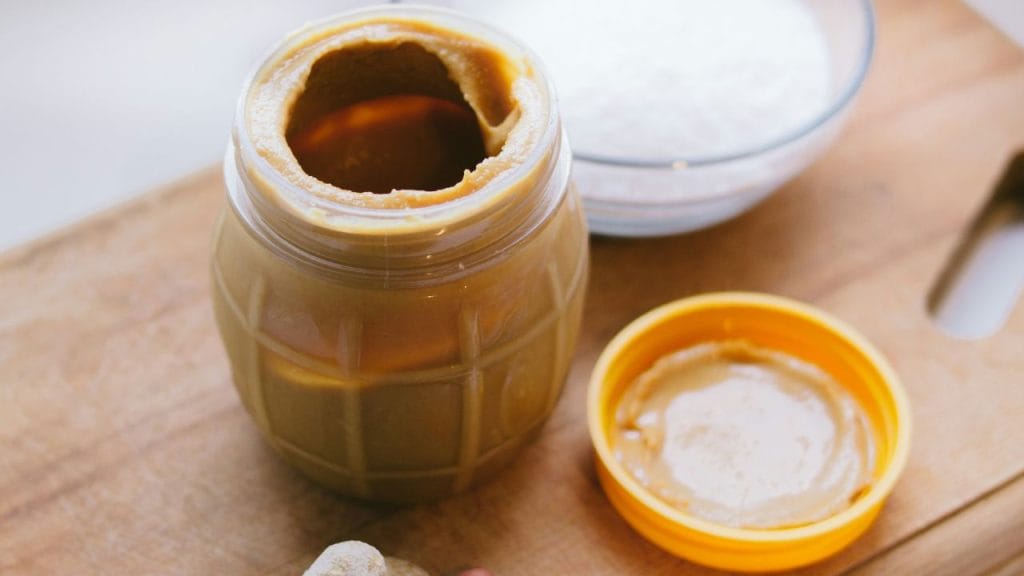 ein offenes Glas Erdnussbutter mit seinem Deckel