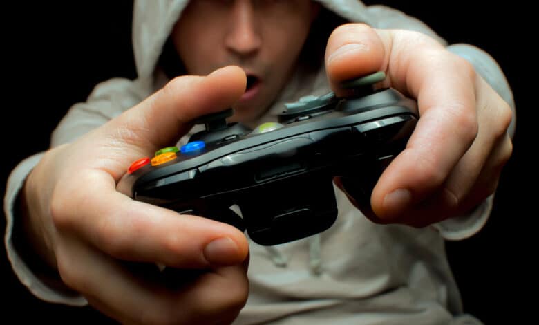 uomo che gioca con un controller nero e che indossa un cappuccio