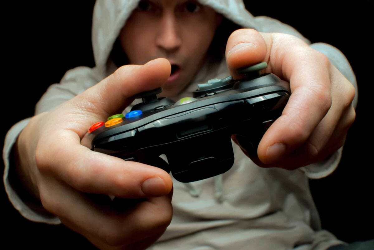 uomo che gioca con un controller nero e che indossa un cappuccio