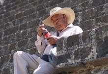 un uomo messicano che guarda una bottiglia di coca cola seduto su un gradino di pietra