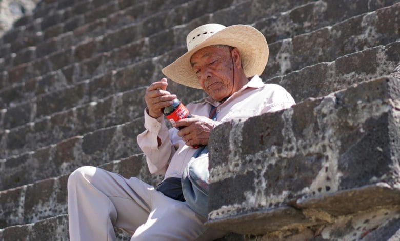 un uomo messicano che guarda una bottiglia di coca cola seduto su un gradino di pietra