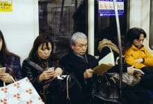 persone di etnia asiatica sedute sulla metro che stanno leggendo smartphone o libri