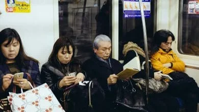 persone di etnia asiatica sedute sulla metro che stanno leggendo smartphone o libri