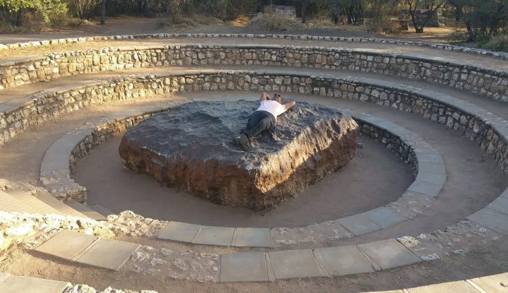 un uomo sdraiato sul meteorite hoba in namibia, per far vedere quanto è grande la roccial