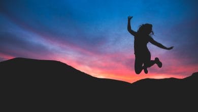 una donna che salta felice con in background un tramonto rosa sul cielo blu