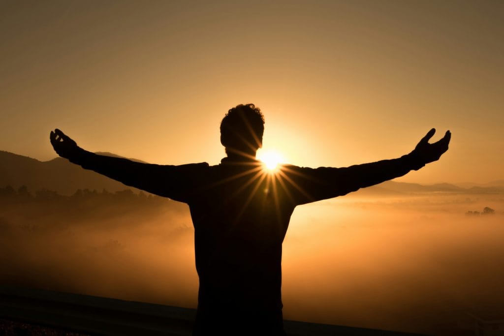 uomo con le braccia alzate come se volesse abbracciare il sole, con il sole nascosto dietro la sua sagoma